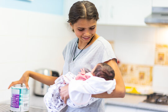 teen girl holding baby with tin of infant formula on kitchen bench