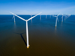 A cluster of wind turbines stands tall in the ocean, the power of the wind as they rotate against...