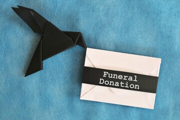 Black raven paper origami carrying white letter money envelope with word Funeral Donation.