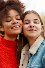 Portrait of two happy multiracial girlfriends smiling at camera while spending time in fall nature, cheerful teen girls of different races