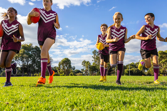 schoolkids running towards the camera on green grass with footballs