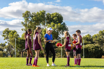smiling female coach holding clipboard addressing schoolchildren in sports uniforms