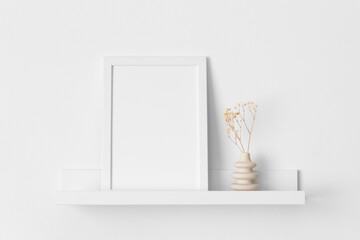 White frame mockup with a gypsophila decoration on the wall shelf.