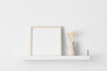 Wooden square frame mockup with a gypsophila decoration on the wall shelf.