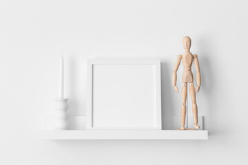 White square frame mockup with manikin and candle decoration on the wall shelf.