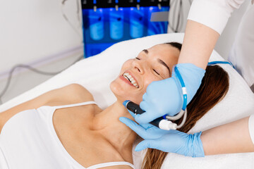 A cosmetologist wearing gloves performs vacuum cleaning and polishing of the facial skin of a...