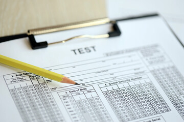 Blank educational test for students lies on table in classroom with pencil close up