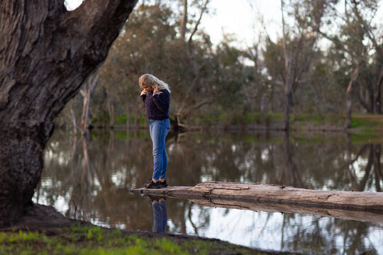 tween girl wearing jeans looking at reflection in water standing on log