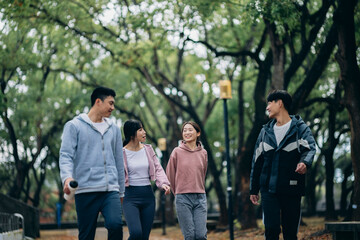 young Asians walk outdoors, sharing their recent exercise experiences as they stroll. They also use...
