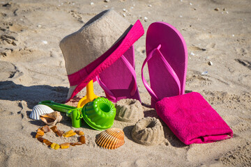 Different shapes made of sand, children toys for playing and accessories for relax. Straw hat, slippers and towel. Summer time on beach