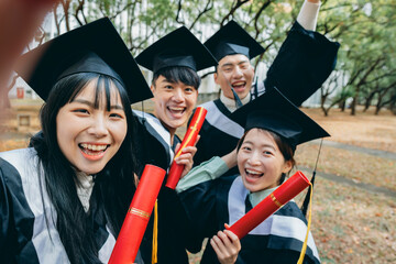 Four Asian graduates happily take a selfie, waving at the camera to capture this precious moment.