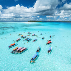 Aerial view of colorful boats in transparent water on sunny day. Mnemba island, Zanzibar. Top view of sandbank in low tide, blue sea, sand, swimming people, yachts, sky with clouds in summer. Ocean - 784413233