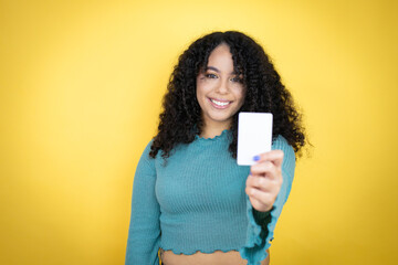 African american woman wearing casual sweater over yellow background smiling and holding white card