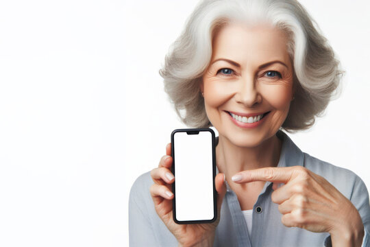 Portrait of a smiling senior woman pointing on smartphone with white screen on white background