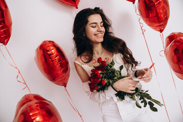 A smiling woman with kisses lipstick is holding a bouquet of red roses and standing amidst...