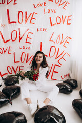 Woman sitting with kisses lipstick hold bouquet of red roses, black foil balloons, the word LOVE...