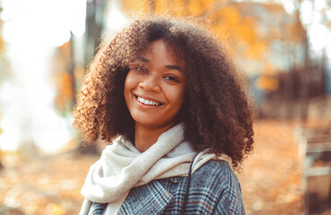 Cute autumn close up portrait of young smiling happy african american woman with curly hair...