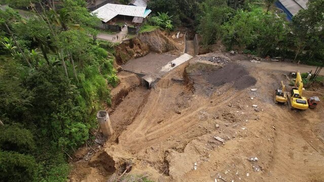 Aerial view of road reconstruction after erosion and landslide at ravine. Concrete box culvert already build, ground works in progress. Camera fly up and back and reveal general view of area.