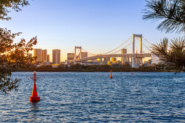 The sunset view of Rainbow Bridge with a buoy in the front in Odaiba, Tokyo, Japan.	