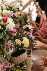 Busy floral arrangement session with hands carefully placing a variety of flowers into a wooden pot.