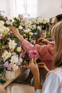 Floral workshop scene with participants arranging pink tulips and pastel flowers.
