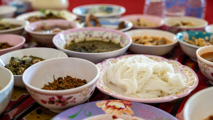 A close-up view of khanom jeen, curry, fried eggs, stir-fries and many other dishes packed in bowls.