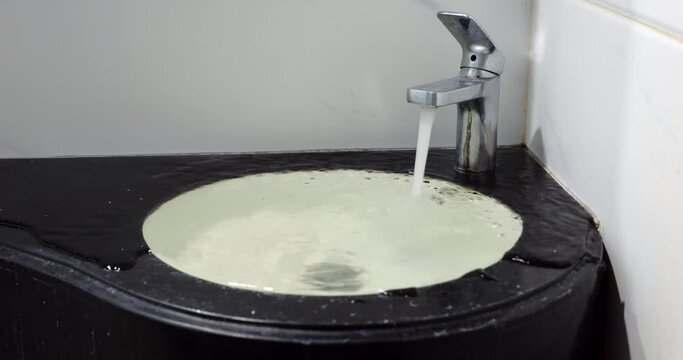 Plumbing issue at apartment or hotel bathroom, water fill up sink and flow out and over countertop. Despite modernistic design, it looks kind of dirty and unkempt, faucet not polished and mold visible