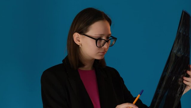 Female doctor in glasses examines X-ray picture on blue background. Female worker eyes scan intricate details with precision