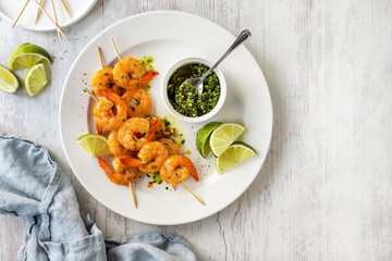 Grilled shrimp skewers served with green herbs pesto and lime slices top view on a plate