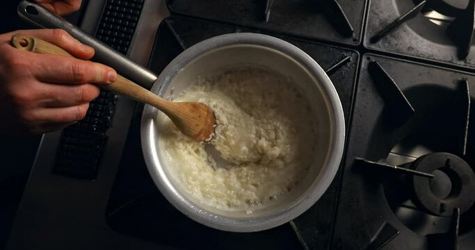 Making Italian Risotto in a Professional Kitchen. Top View of a Chef stirring and mixing rice with wooden spoon. Rice in a pot on top of the stove.