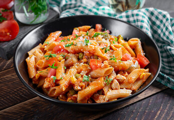Classic italian pasta penne arrabbiata with vegetables on wooden table. Penne pasta with sauce...