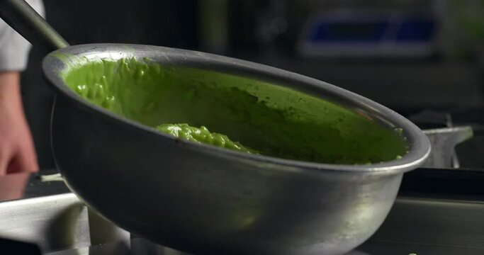 Close up shot of Chef tossing Pesto Risotto in a professional Kitchen. Homemade Green Rice mixed with wooden spoon. Traditional Italian recipe with basil pesto and tossed with butter.
