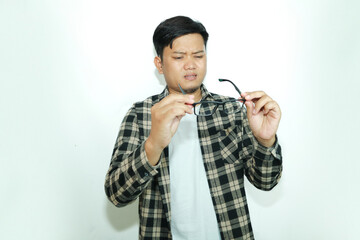 Young Asian man holding glasses with sad expression