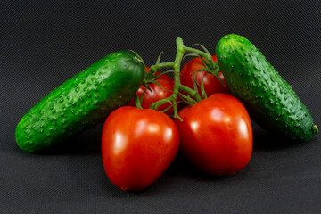 Ripe plum-shaped tomatoes with cucumbers on a black background close-up