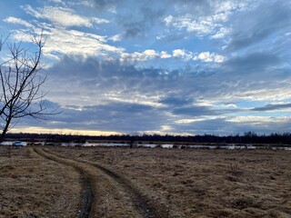 Spring village landscape: sky in the clouds, dry grass on the field and a blue river - 784448679