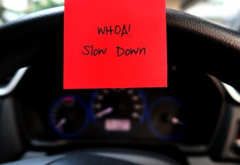 Red sticky note with text written  WHAO! SLOW DOWN  on the car steering wheel , to remind driver to...