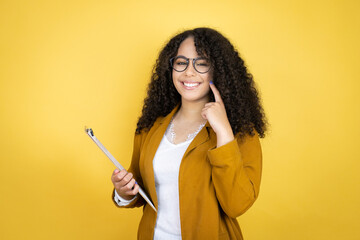 African american business woman with paperwork in hands over yellow background very happy and excited making winner gesture with raised arms, smiling and screaming for success.