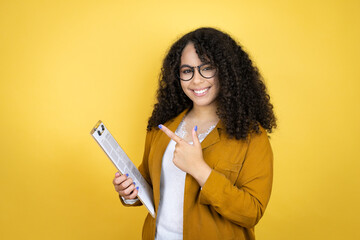 African american business woman with paperwork in hands over yellow background amazed and pointing with hand and finger