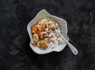 Delicious breakfast - cottage cheese with greek yogurt, banana, crackers and chocolate on a dark background, top view - 784472079