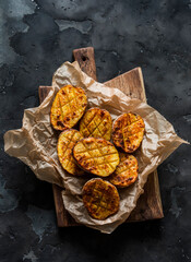 Crispy grilled potatoes on a rustic wooden chopping board on a dark background, top view