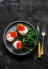 Delicious tapas, appetizer - grilled potatoes with sour cream and red caviar and arugula salad on a dark background, top view