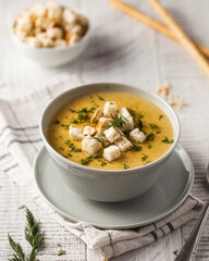 Homemade creamy cheese soup topped with croutons and dill, served in a grey bowl