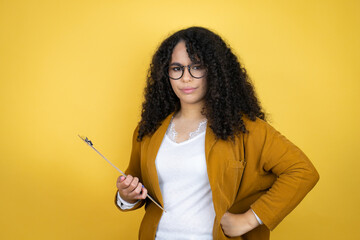 African american business woman with paperwork in hands over yellow background skeptic and nervous, disapproving expression on face with arms in waist - obrazy, fototapety, plakaty