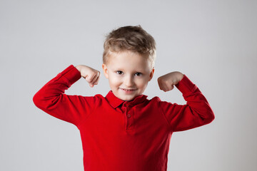 A young boy showing off his muscles while wearing a red shirt
