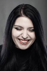 Portrait of a goth style girl smiling with closed eyes against gray background