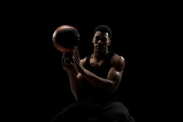 Basketball player spinning a ball against black background. Muscular african american man sidelit silhouette.