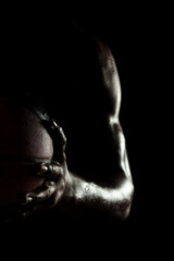 Basketball player holding a ball against black background. Abstract wet male body of african american man. Muscular person sidelit silhouette.