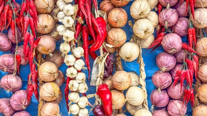 Rows of garlic and chili peppers are strung up against vibrant blue backdrop, creating a bold and...