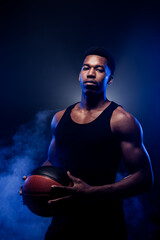 Basketball player holding a ball against blue fog background. Muscular african american man with basket ball