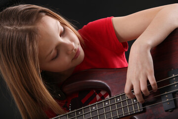 Fototapeta na wymiar preteen girl playing bass guitar on black background